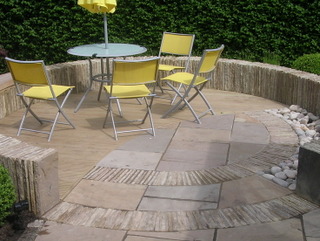 stone circular seating area with yellow chairs garden umberella and round table decking cobbles paving and low stone wall contemporary garden design