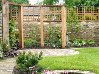 small yorkshire garden with timber pergola in corner and circular patio for outdoor seating