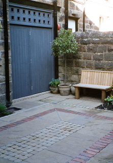 courtyard garden landscaping with new courtyard gates built in seating and simple timber seat brick paving detail in stone paving and setts at Otley Yorkshire