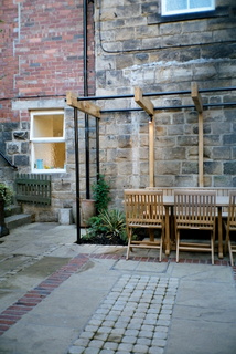 courtyard garden landscaping with brick paving detail in stone paving and setts detail dining table under metal and timber simple pergola at Otley Yorkshire