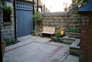courtyard garden landscaping with built in seating and simple timber seat sett and brick paving patters in stone paving  at Otley Yorkshire