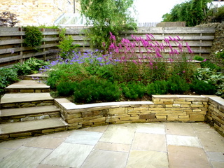 low stone retaining wall flower bed and stone steps curve up garden timber fence